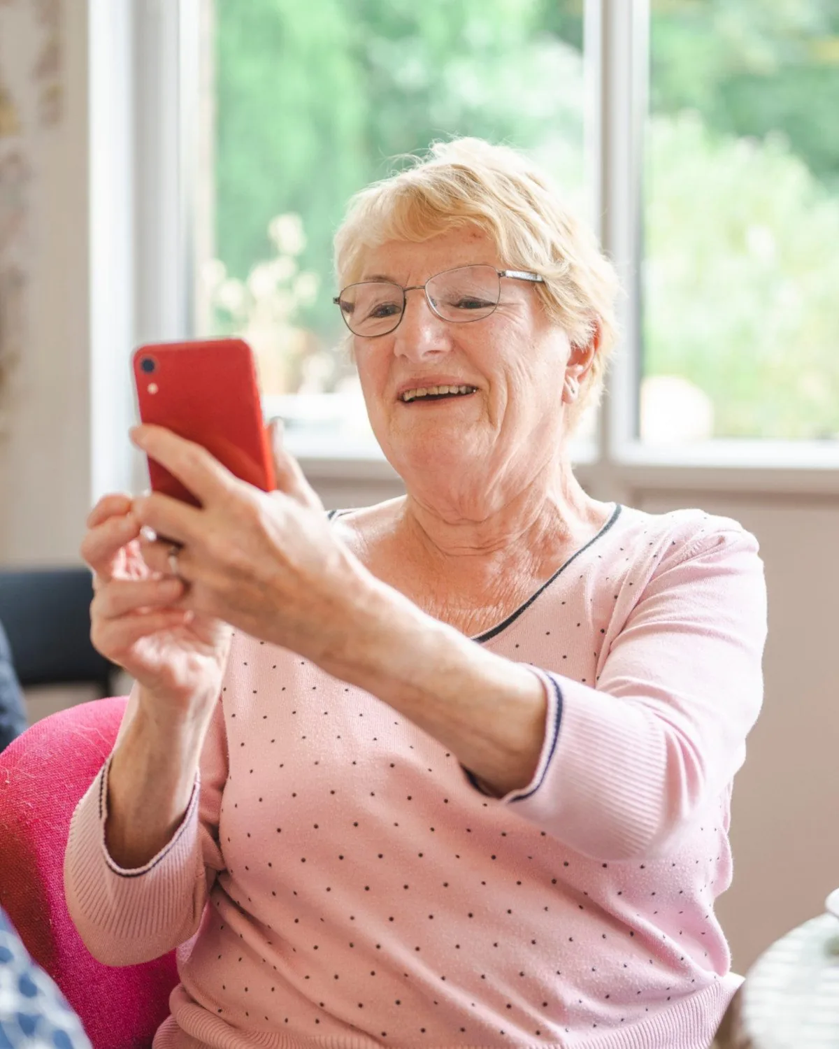 An older woman smiling as she reads her phone at home.